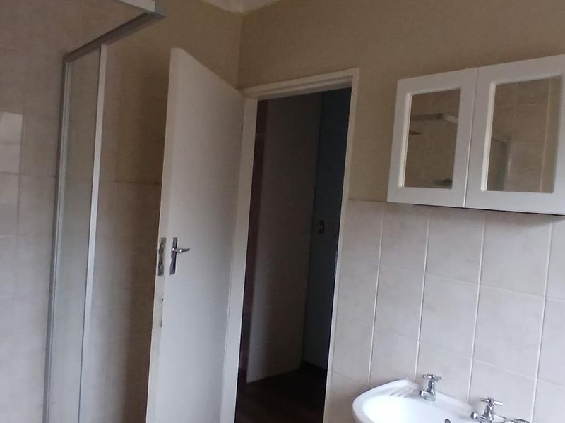 A functional bathroom featuring a shower enclosure, pedestal basin, and wall-mounted storage cabinet with neutral wall tiling.