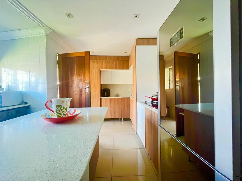 A modern kitchen featuring a central island with stone countertops, light wood cabinetry, and tiled flooring, offering a functional and bright workspace.