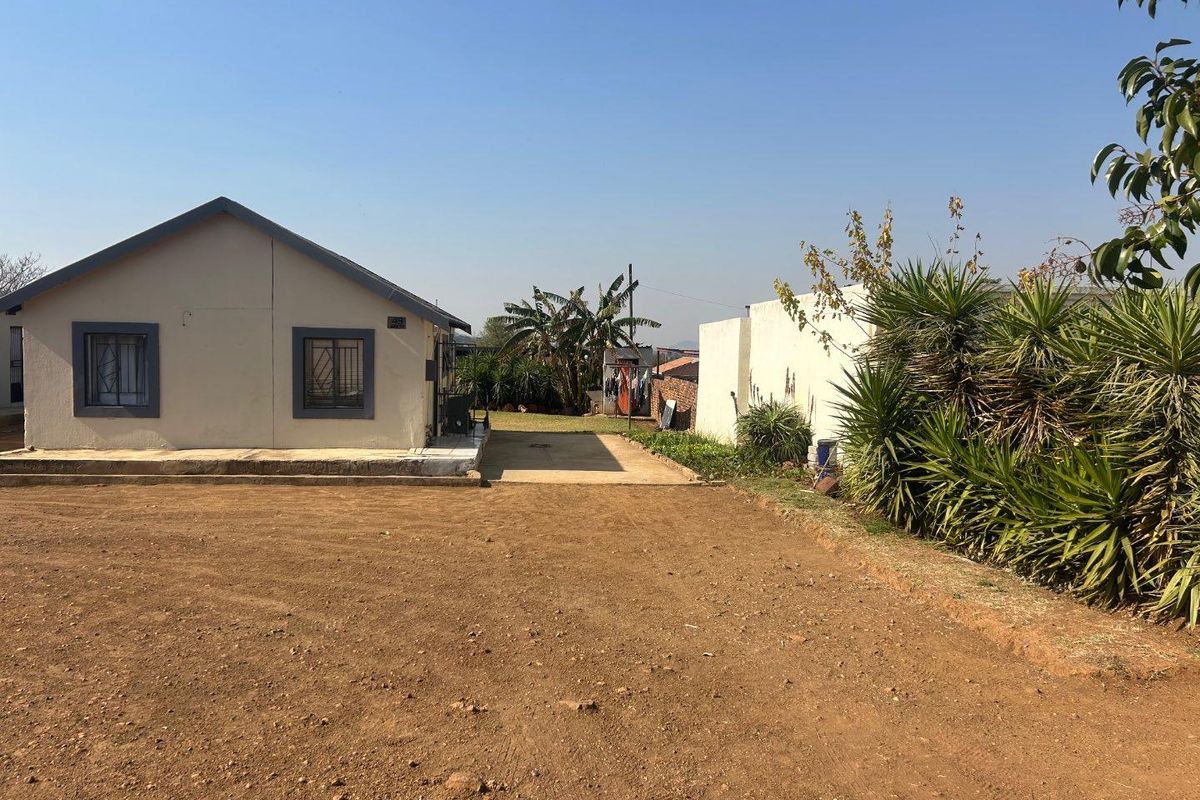 A view of the rear exterior of the house featuring a concrete patio area and a large unpaved yard with established perimeter landscaping.