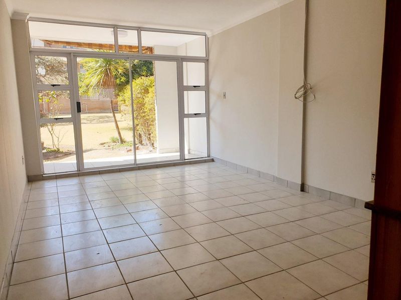 An empty, tiled living room featuring large sliding glass doors that provide natural light and direct access to the outdoor area.