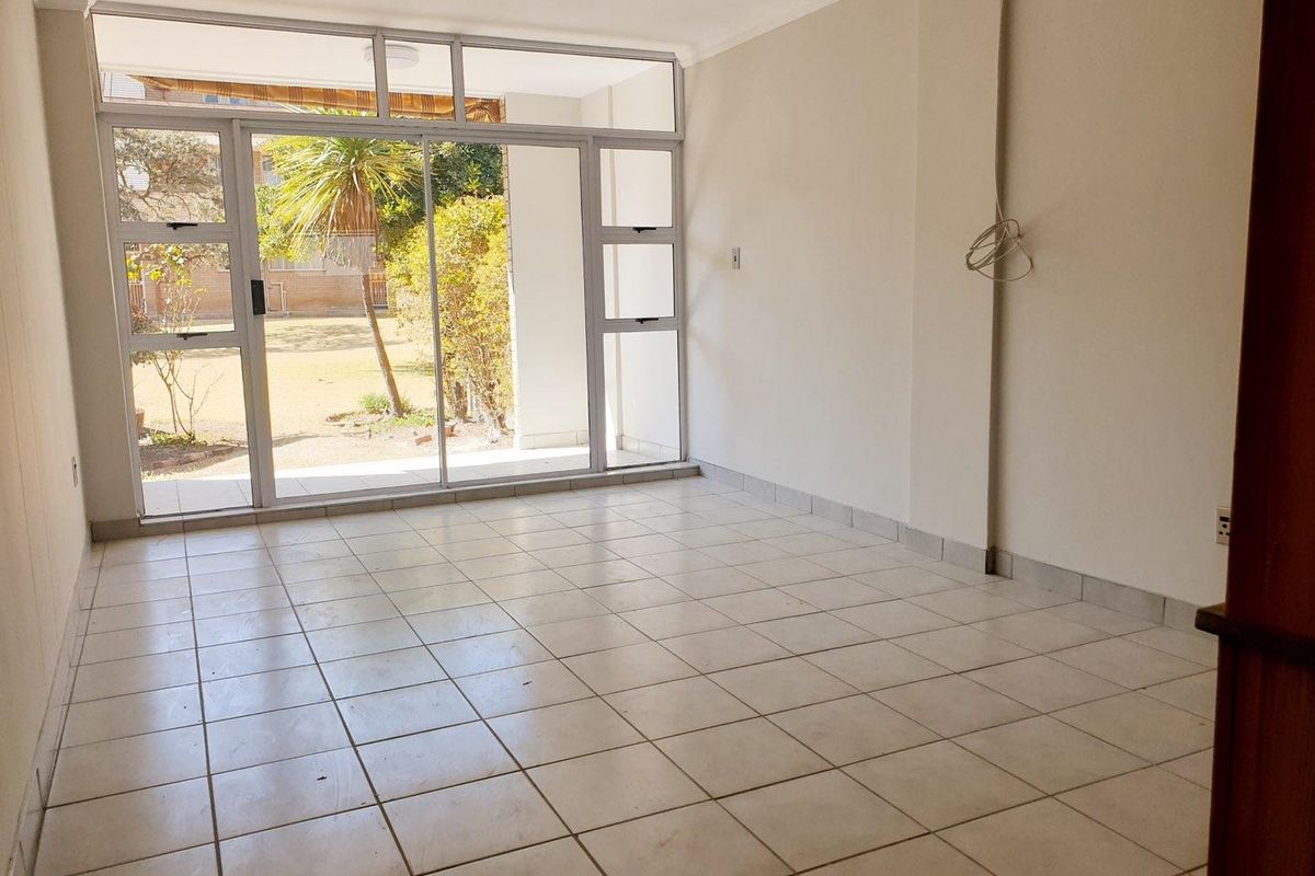 An empty, tiled living room featuring large sliding glass doors that provide natural light and direct access to the outdoor area.