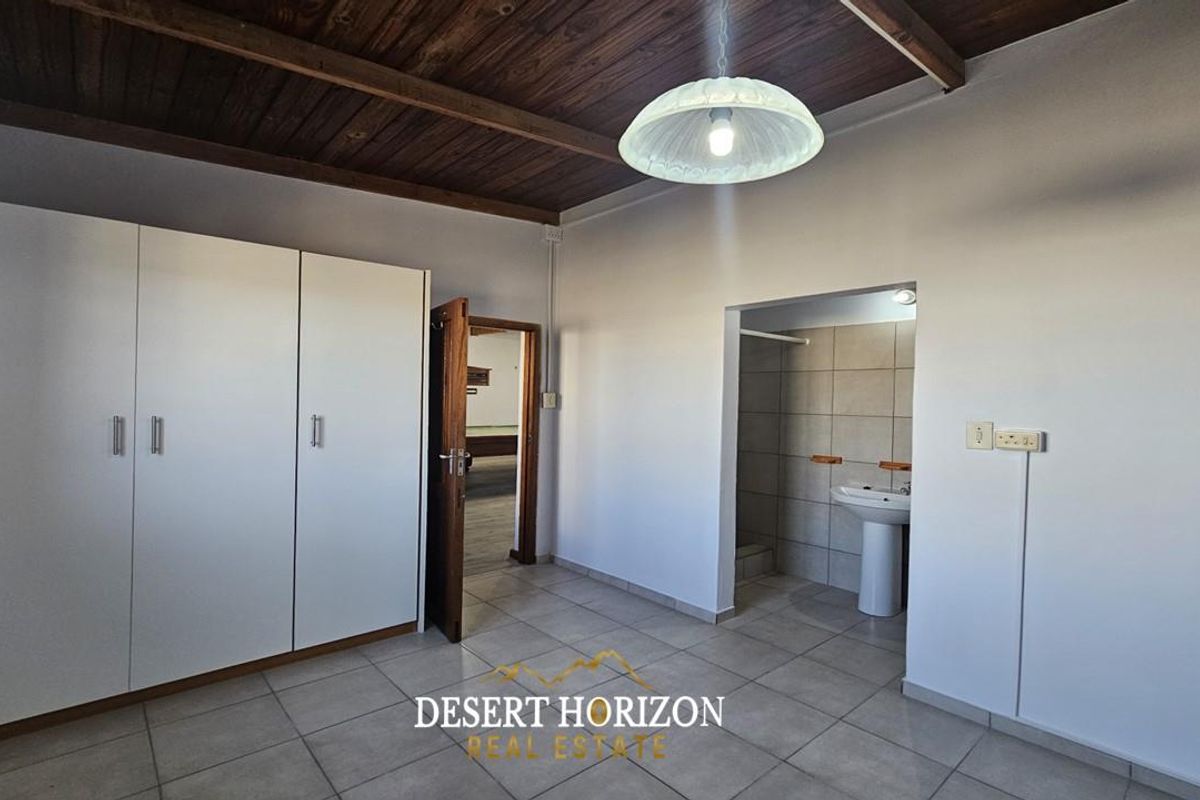 Bedroom featuring built-in cupboards, tiled flooring, exposed timber beam ceiling, and an en-suite bathroom area with a pedestal basin.