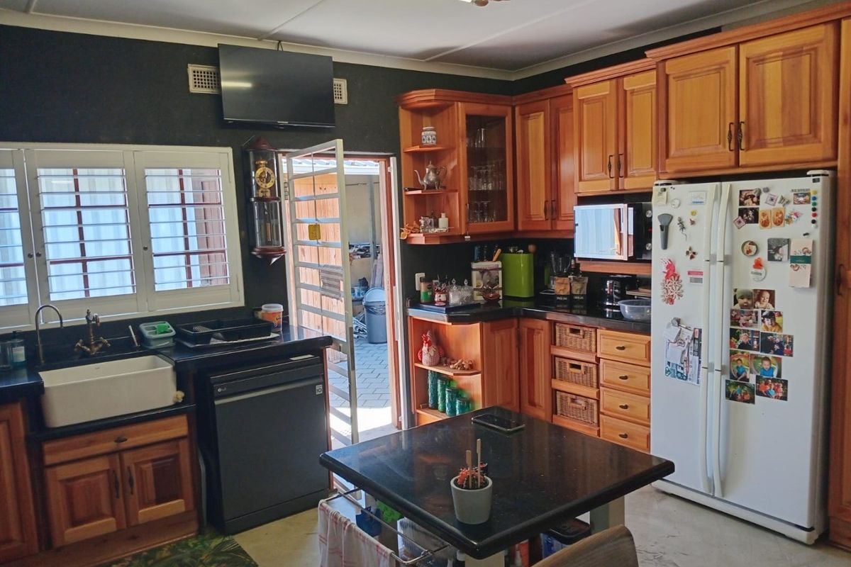 A functional kitchen featuring warm wooden cabinetry, granite countertops, a farmhouse sink, and direct access to an outdoor area.