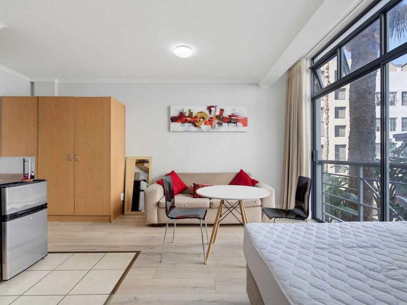 Open-plan studio apartment featuring laminate flooring, a tiled kitchen area, and a large sliding glass door leading to a balcony.