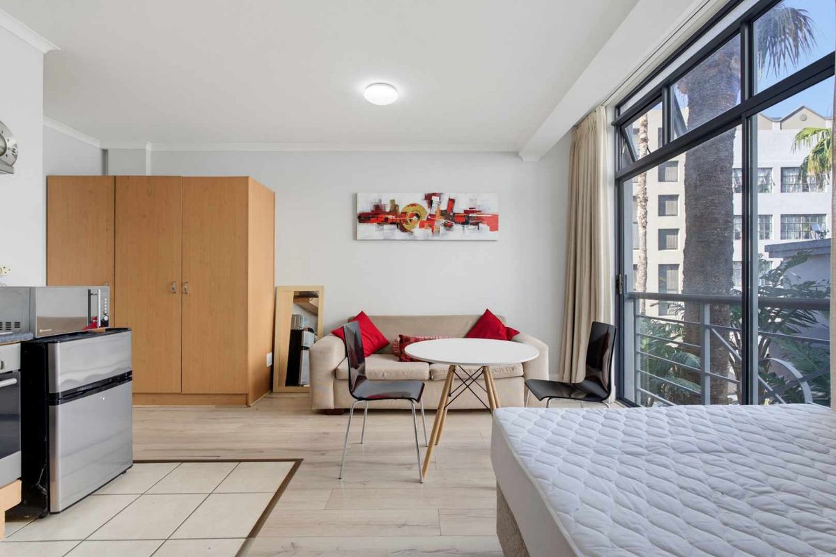 Open-plan studio apartment featuring laminate flooring, a tiled kitchen area, and a large sliding glass door leading to a balcony.