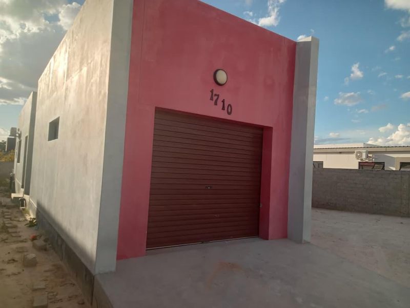 A detached garage structure featuring a brown roller shutter door and a pink facade, situated on a concrete driveway.