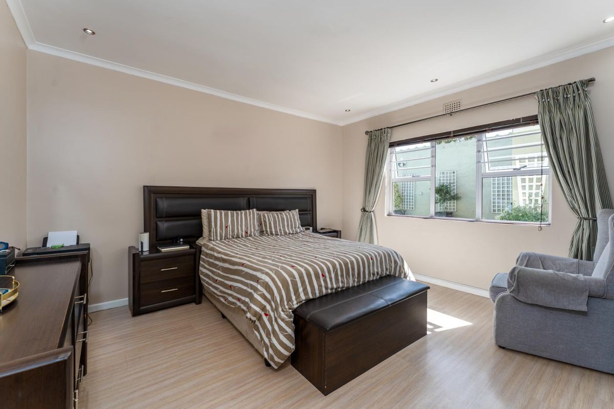 A well-maintained bedroom featuring light wood-look flooring, neutral wall tones, recessed ceiling lighting, and large windows allowing for natural light.