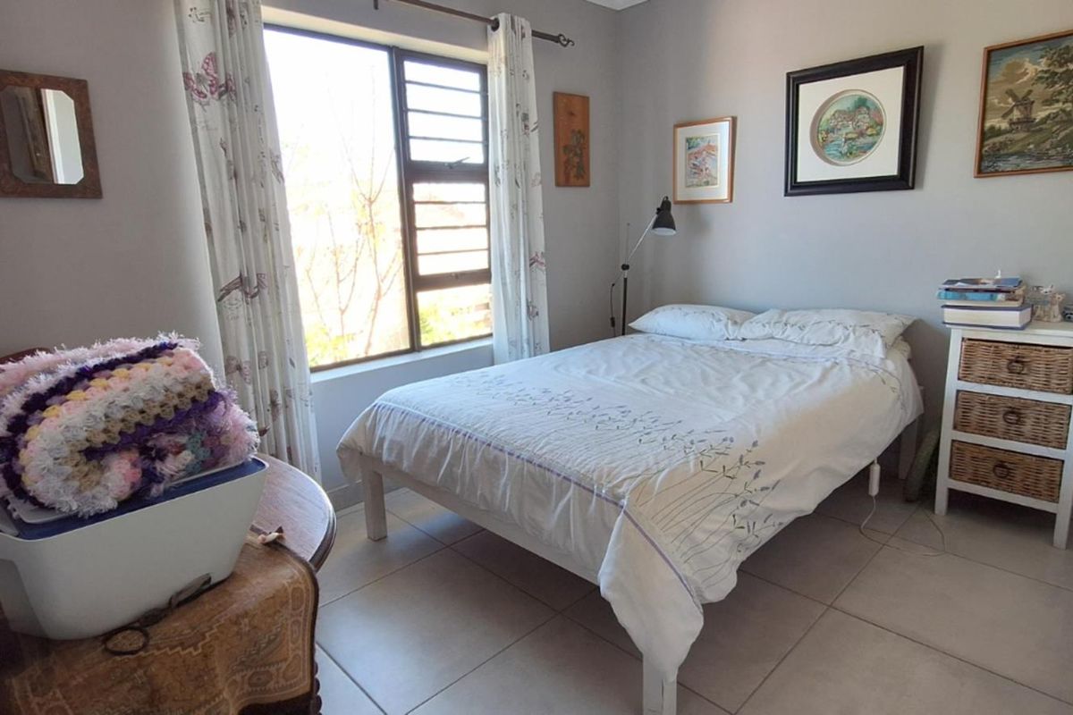 A functional bedroom featuring tiled flooring, a large window for natural light, and built-in wardrobe storage.