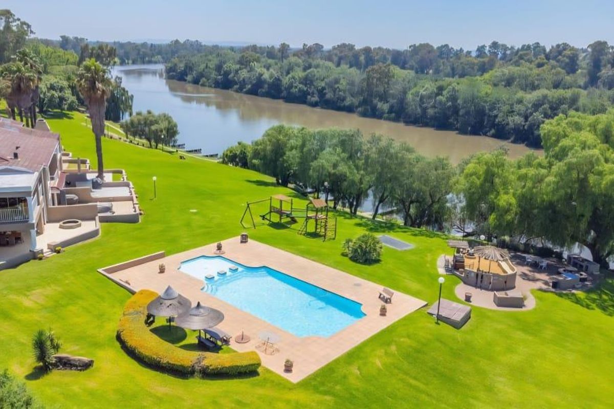 Aerial view of a townhouse property featuring a large swimming pool, expansive landscaped garden, and direct river frontage with outdoor entertainment facilities.