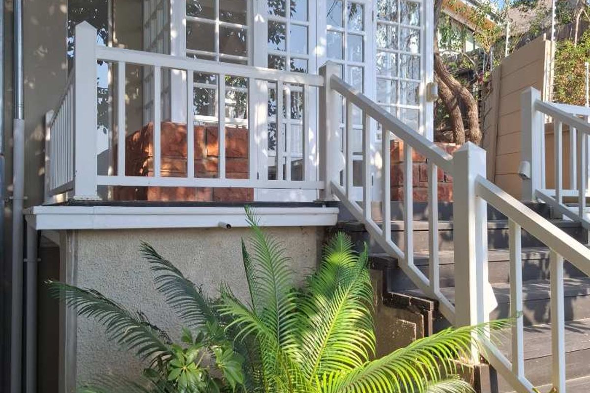 A rear exterior view featuring a charming glass-enclosed sunroom with a white timber staircase and balustrade leading up to the structure.