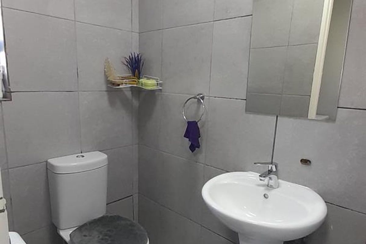 A compact guest bathroom featuring full-height grey wall tiling, a white pedestal basin, and a standard toilet.