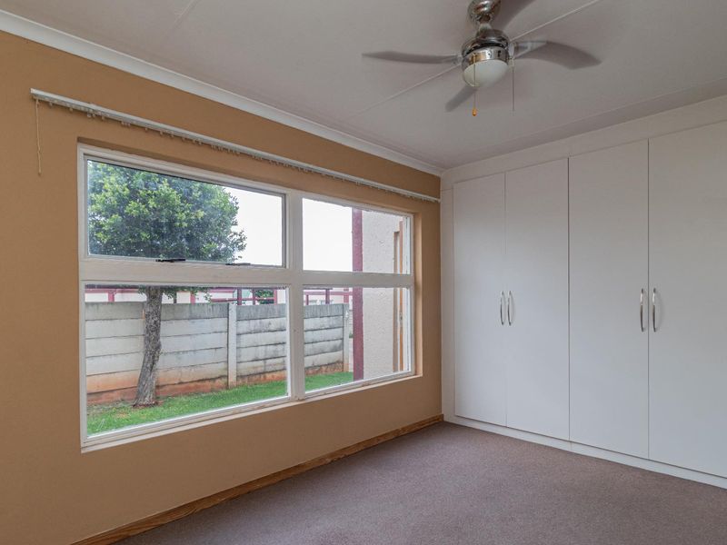 A bright, empty bedroom featuring built-in cupboards, a ceiling fan, and carpeted flooring, offering a clean canvas for personalization.