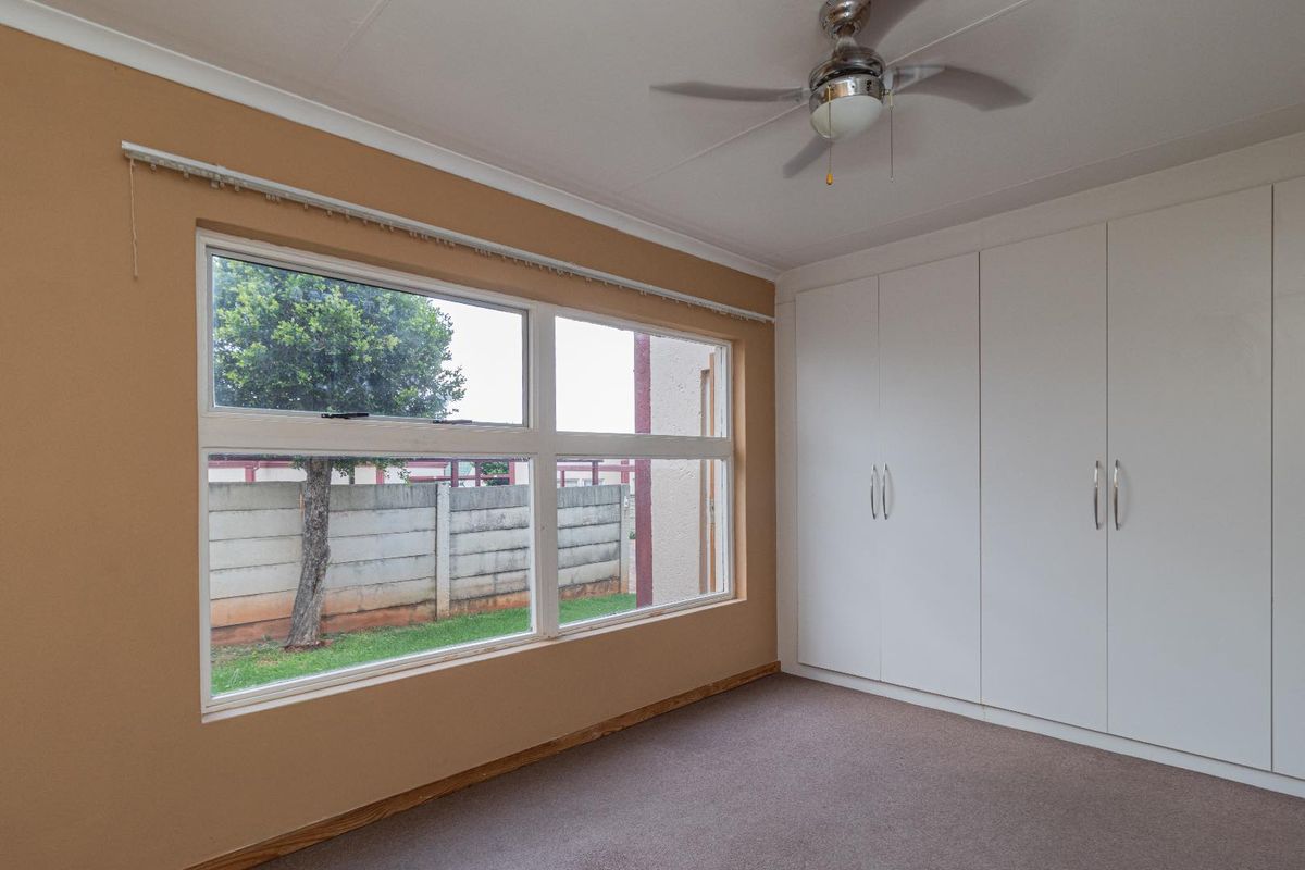 A bright, empty bedroom featuring built-in cupboards, a ceiling fan, and carpeted flooring, offering a clean canvas for personalization.