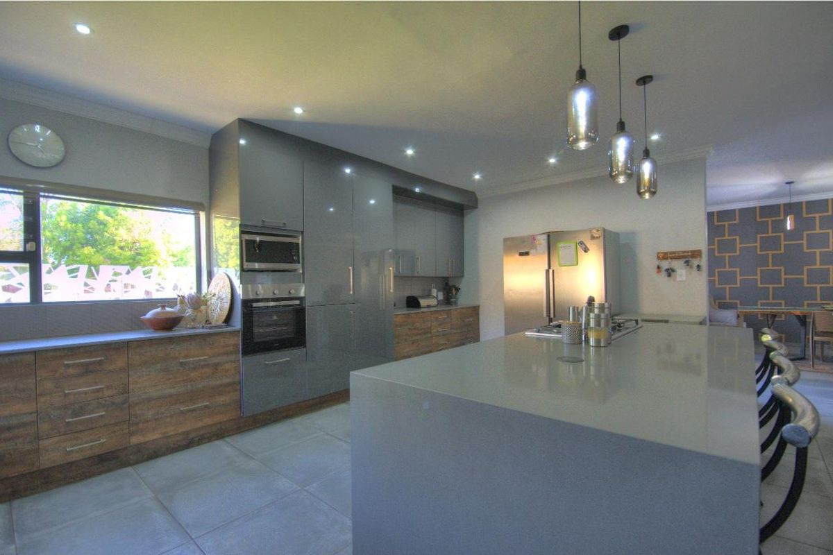 Modern kitchen featuring a large central island, stone countertops, built-in oven and microwave, and sleek cabinetry with integrated lighting.