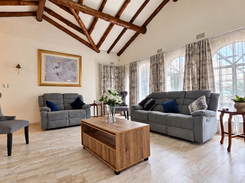 Spacious living room featuring a vaulted ceiling with exposed timber beams, tiled flooring, and large arched windows that provide ample natural light.