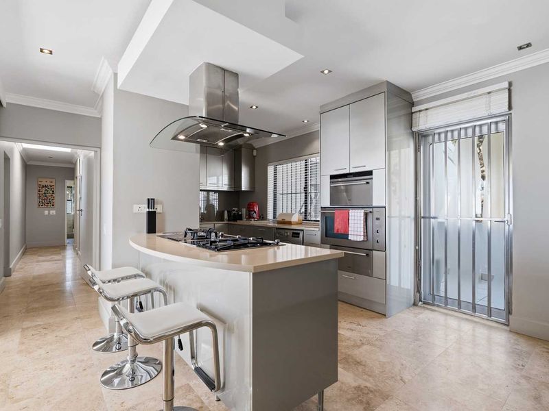 Modern kitchen featuring a central island with gas cooktop, integrated stainless steel appliances, stone countertops, and elegant travertine flooring.