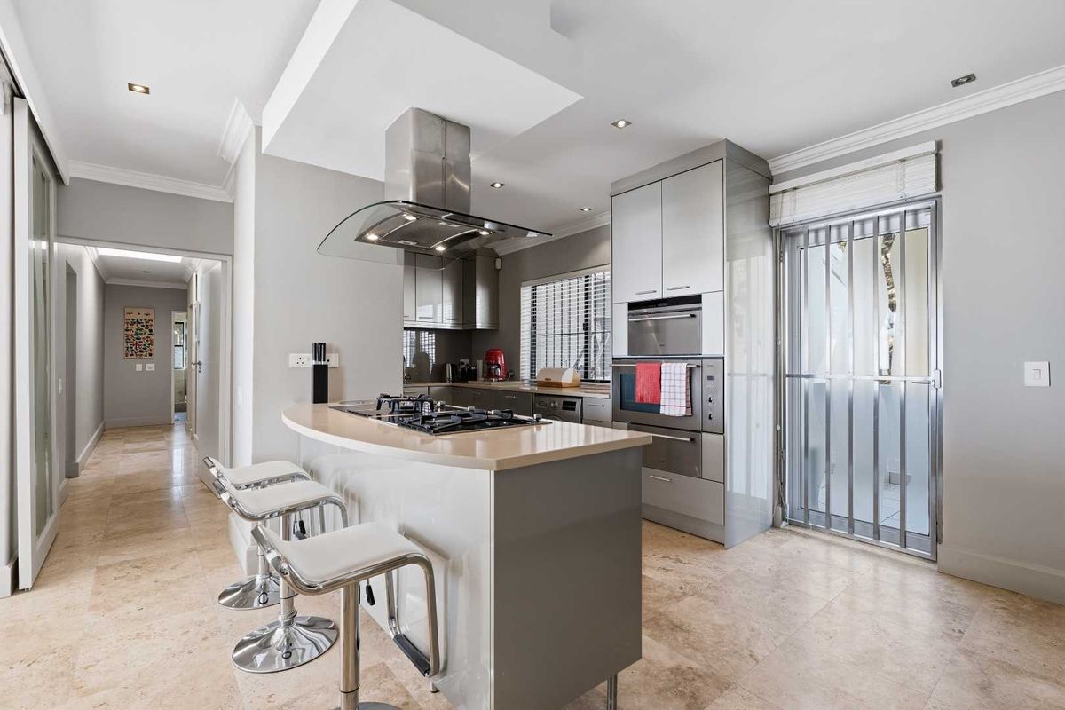 Modern kitchen featuring a central island with gas cooktop, integrated stainless steel appliances, stone countertops, and elegant travertine flooring.