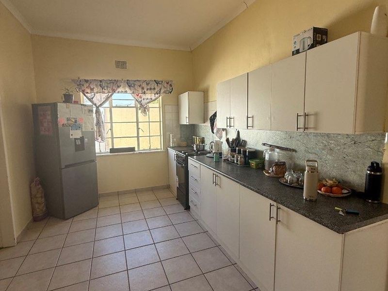 A functional kitchen featuring white cabinetry, laminate countertops, tiled flooring, and a window, offering a practical layout with potential for cosmetic updates.