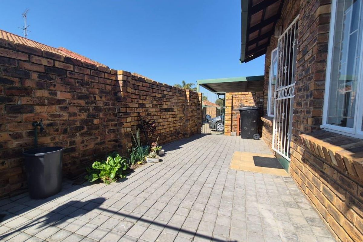 A private rear courtyard featuring paved flooring, face brick boundary walls, and a secure gated entrance leading to a carport area.