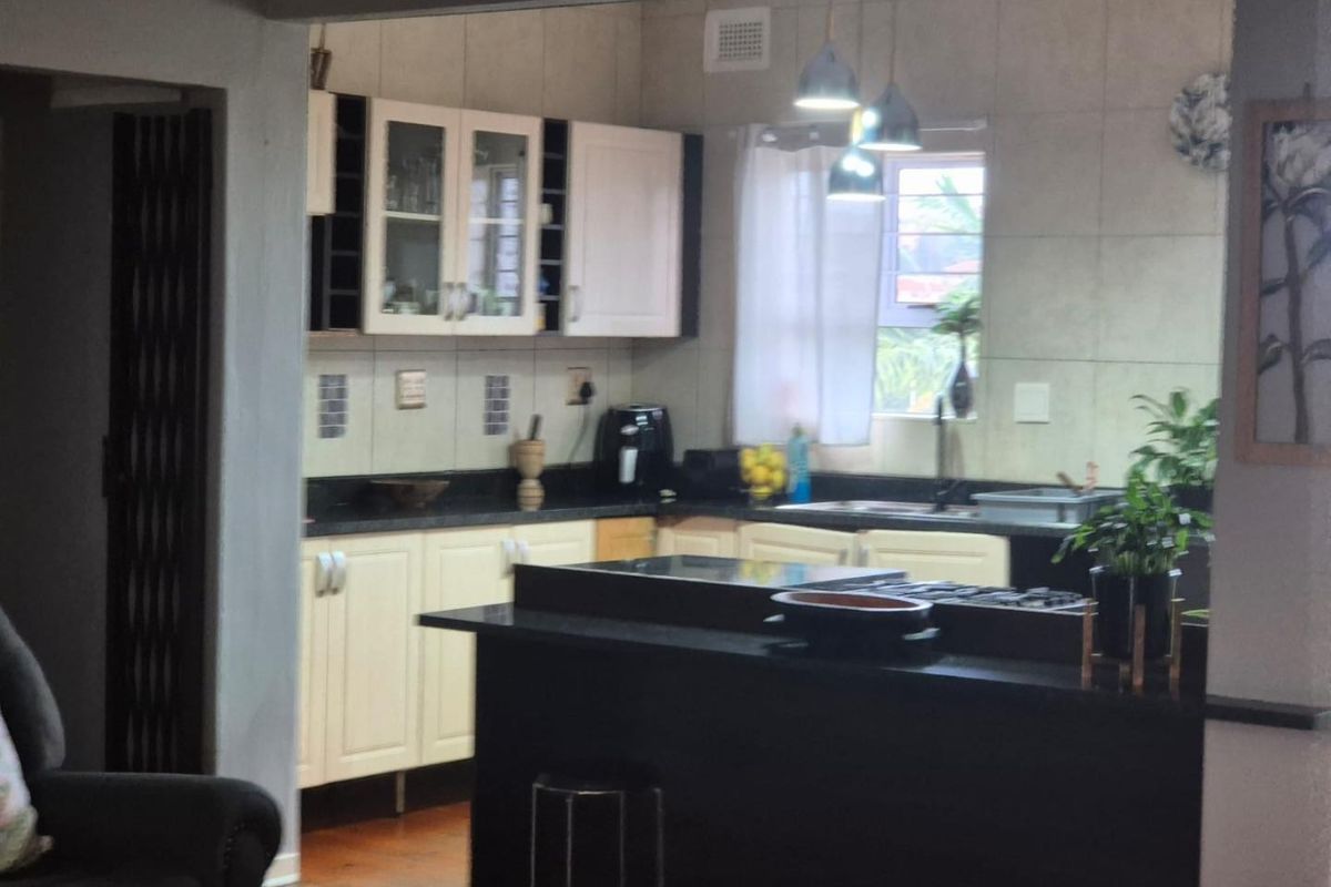 A functional kitchen featuring dark granite countertops, light-toned cabinetry, a central island with a built-in hob, and tiled backsplash.