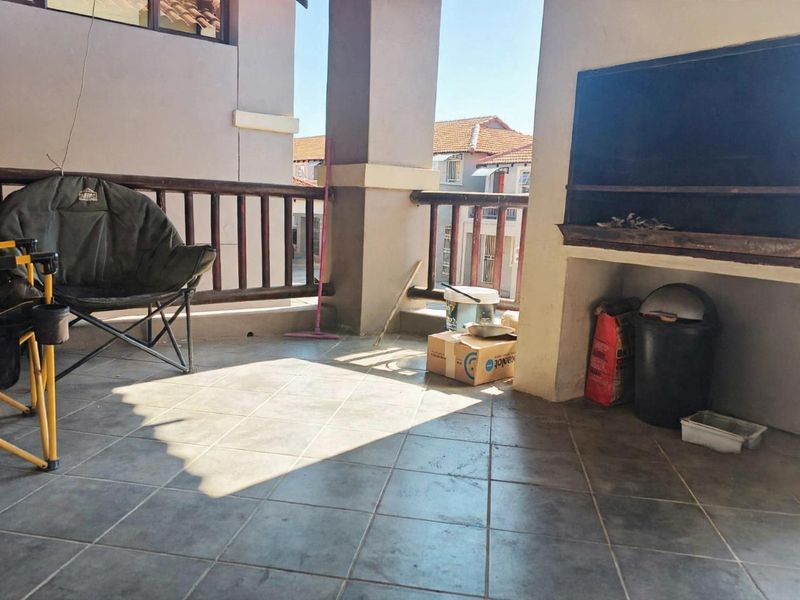A covered patio area featuring a built-in braai, tiled flooring, and a wooden balustrade, offering a functional outdoor entertainment space.