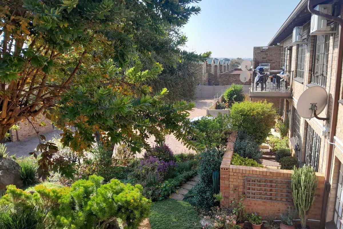 Elevated view overlooking a landscaped garden area with brick retaining walls and a balcony attached to the apartment building.