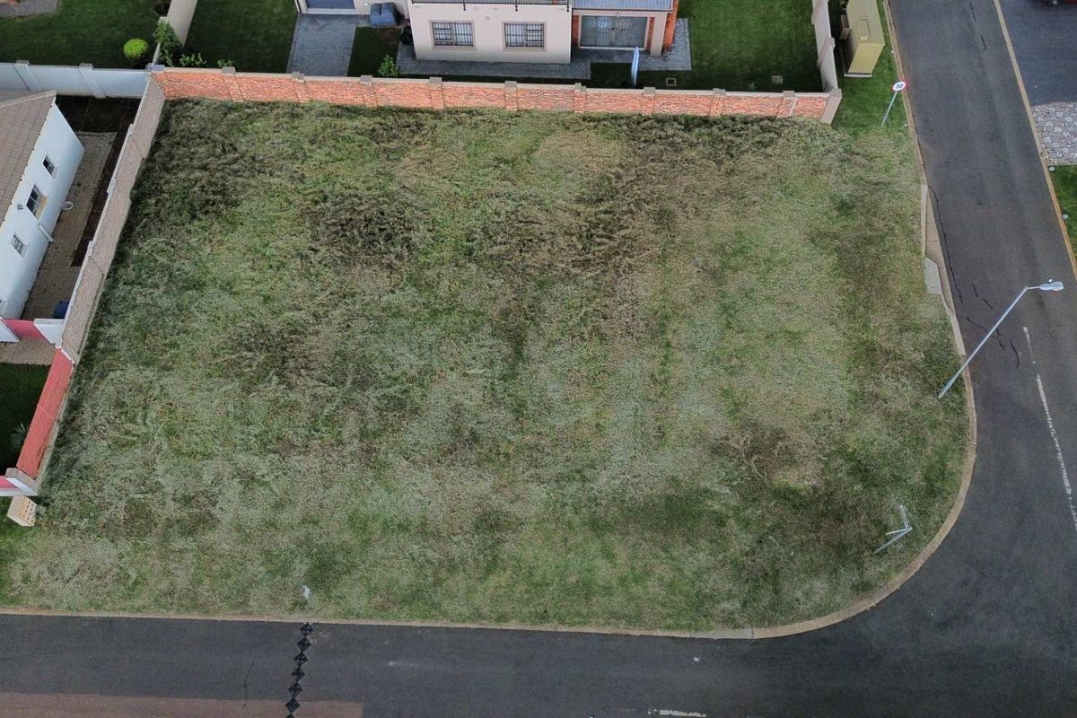 Aerial view of a vacant residential plot featuring established boundary walls and direct street access in a developed neighborhood.