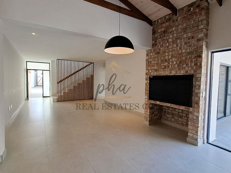 Spacious open-plan living area featuring a striking brick fireplace, exposed timber beams, and modern tiled flooring with direct access to the patio.
