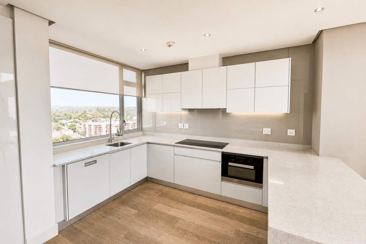 Modern, minimalist kitchen featuring white gloss cabinetry, stone countertops, integrated appliances, and large windows offering expansive city views.