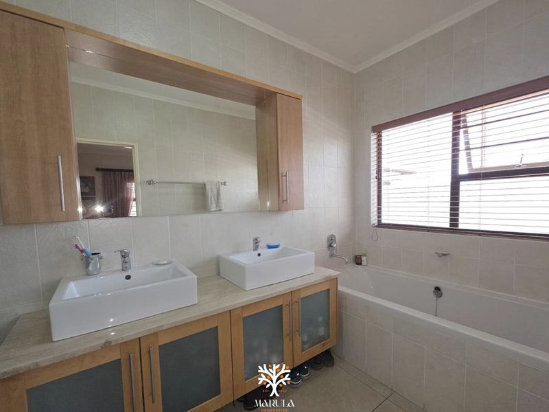 A well-maintained bathroom featuring a double vanity with vessel sinks, built-in cabinetry, and a tiled bathtub area with natural light.