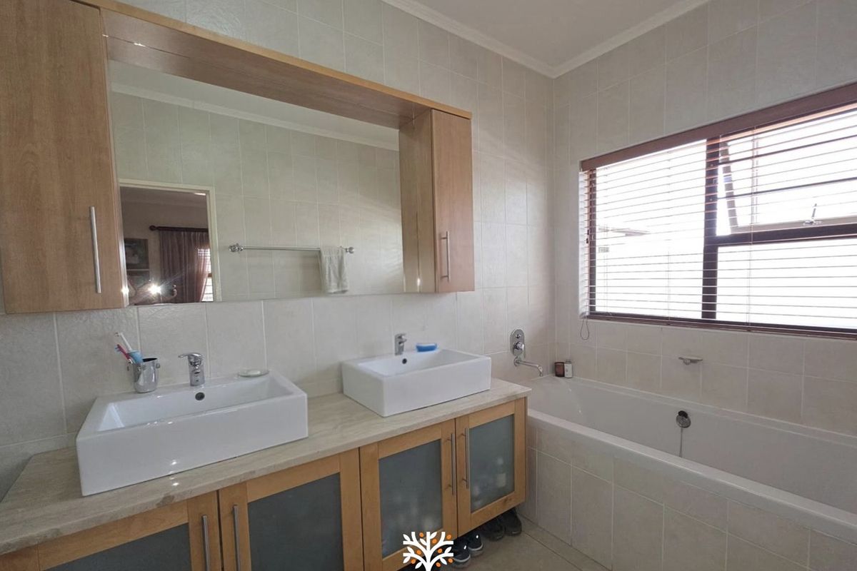 A well-maintained bathroom featuring a double vanity with vessel sinks, built-in cabinetry, and a tiled bathtub area with natural light.