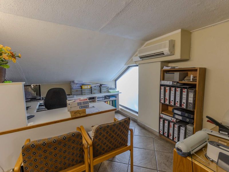 A functional home office space featuring tiled flooring, a sloped ceiling, and a wall-mounted split-system air conditioner.