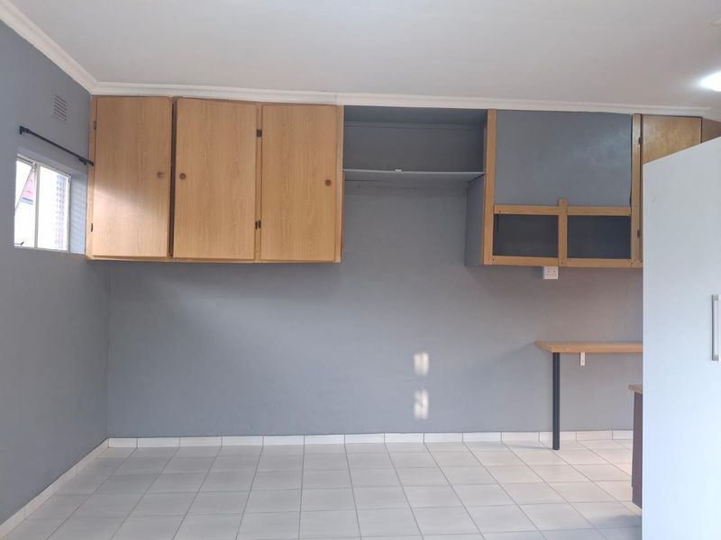 A vacant kitchen area featuring built-in wooden cabinetry, tiled flooring, and a fixed breakfast bar, offering a blank canvas for renovation.