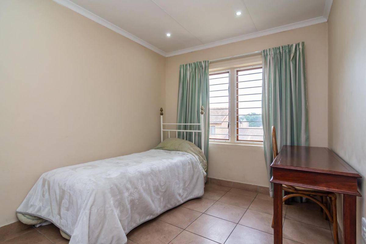 A functional bedroom featuring tiled flooring, recessed downlighting, and a window fitted with security bars.