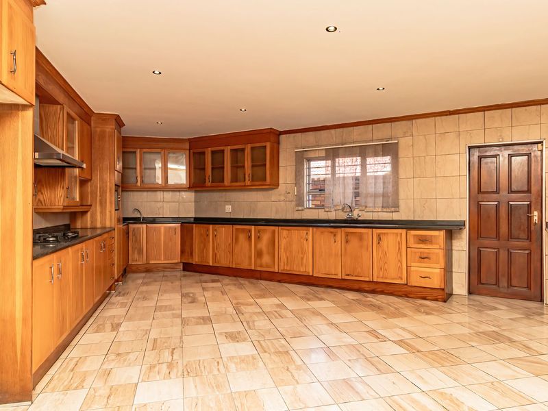Spacious kitchen featuring extensive wooden cabinetry, granite countertops, built-in hob, extractor fan, and tiled flooring throughout.