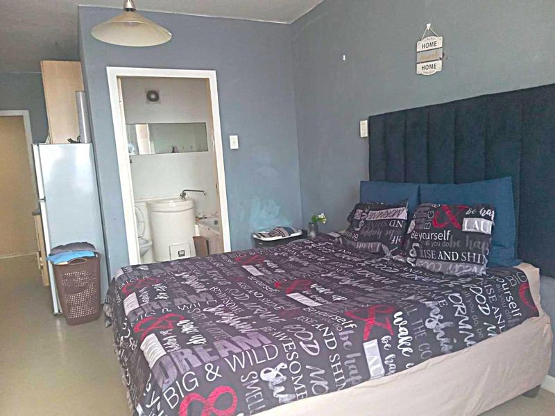 A bedroom featuring tiled flooring and an en-suite bathroom, showing signs of wear on the walls requiring maintenance.