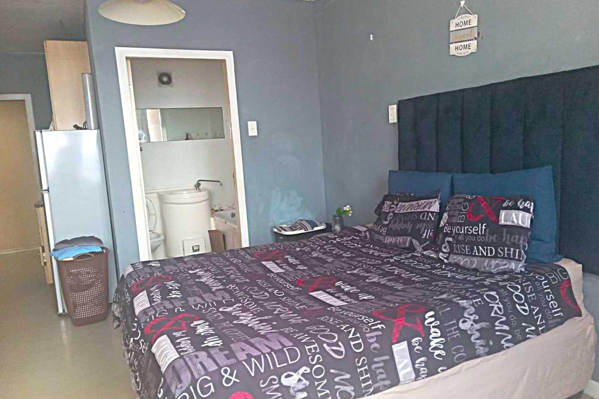 A bedroom featuring tiled flooring and an en-suite bathroom, showing signs of wear on the walls requiring maintenance.