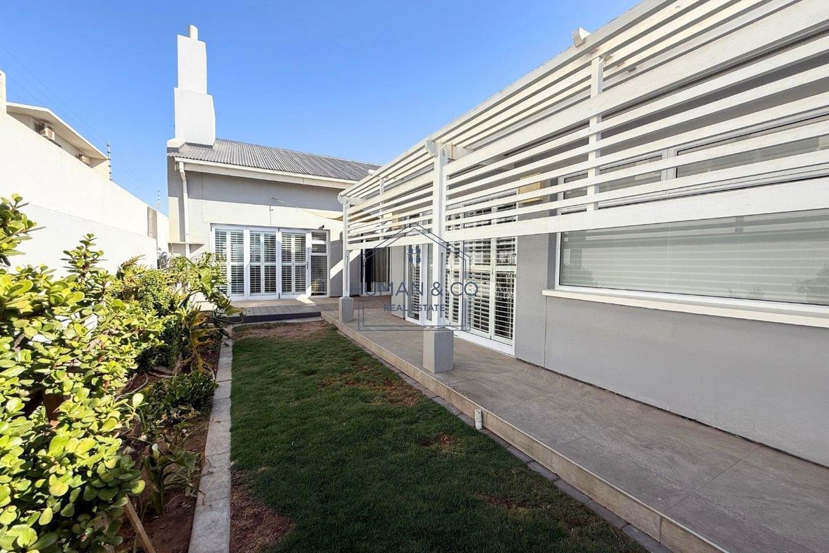 A well-maintained rear exterior featuring a covered patio with slatted timber screening, tiled flooring, and a small landscaped garden area.