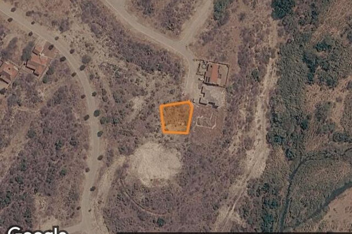 An aerial view of a vacant residential plot highlighted in an estate setting, showing surrounding terrain and access roads.