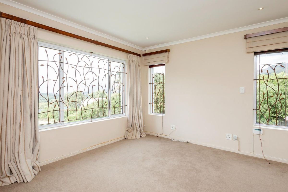 A bright, empty bedroom featuring neutral carpeting, recessed lighting, and large windows fitted with decorative metal security bars.