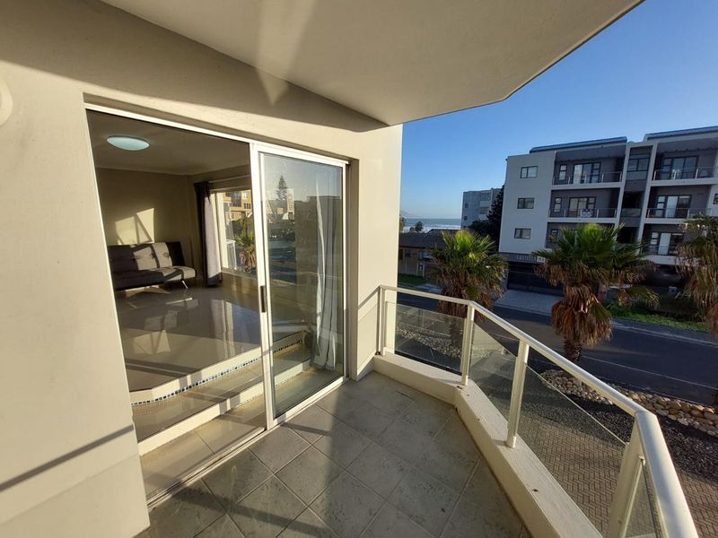 A clean, tiled balcony featuring a modern glass balustrade and sliding door access to the interior living space.