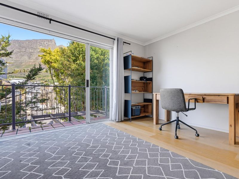 A bright bedroom featuring hardwood flooring and a large sliding glass door that opens onto a balcony with mountain views.