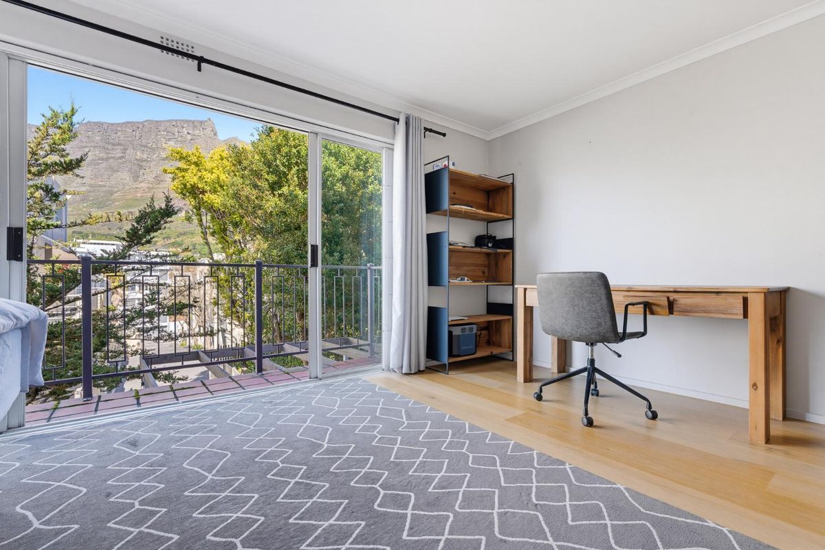 A bright bedroom featuring hardwood flooring and a large sliding glass door that opens onto a balcony with mountain views.