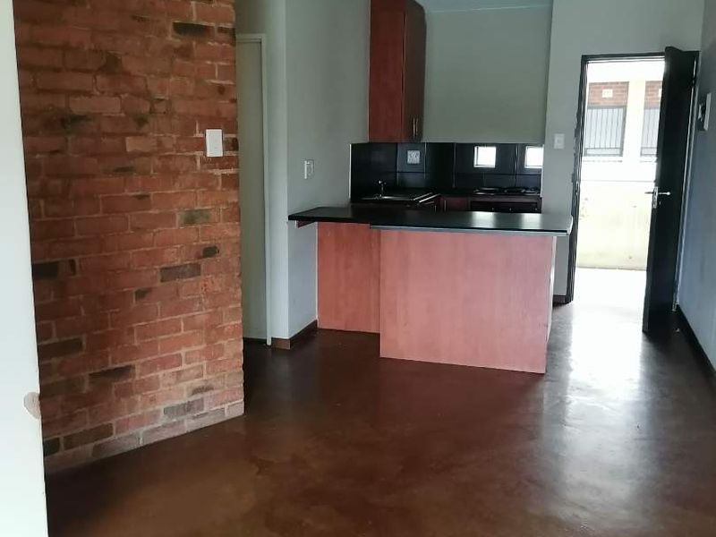 Open plan living area featuring an exposed brick wall, polished concrete floors, and a functional kitchen with built-in cabinetry and appliances.