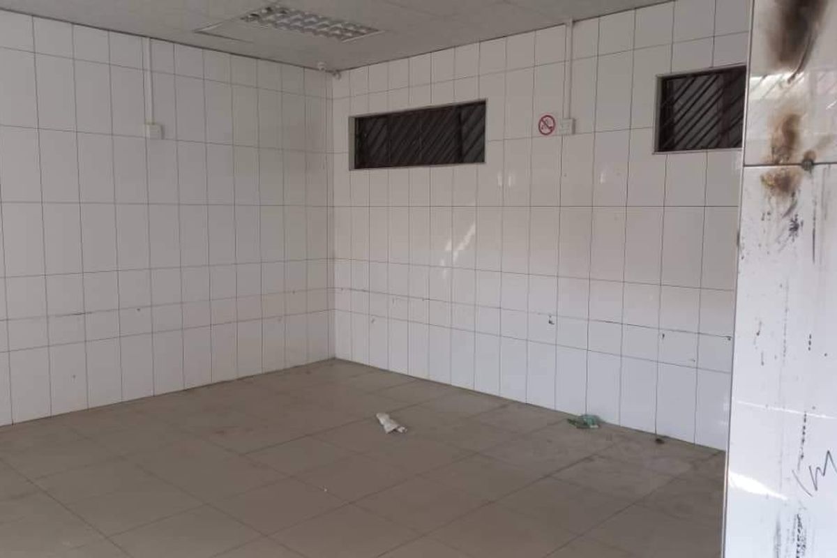 An empty industrial utility space featuring fully tiled walls and floors, recessed lighting, and high-level windows, currently showing signs of fire damage.