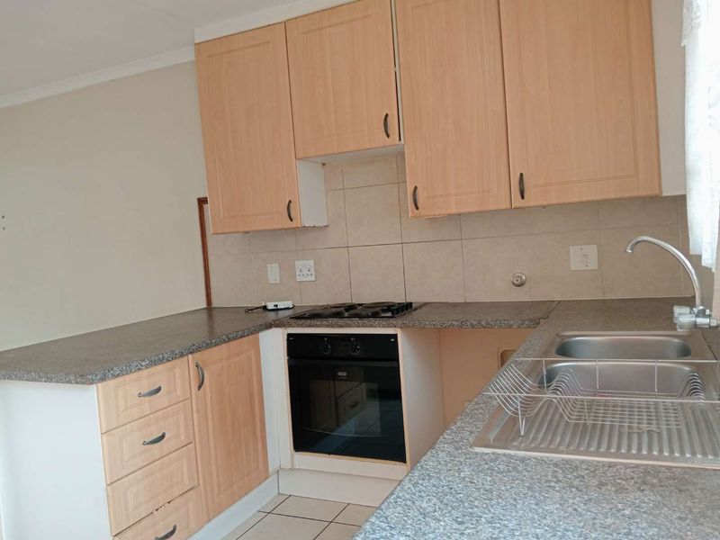 A functional kitchen featuring light wood-finish cabinetry, granite-look countertops, a built-in oven with gas hob, and a double stainless steel sink.
