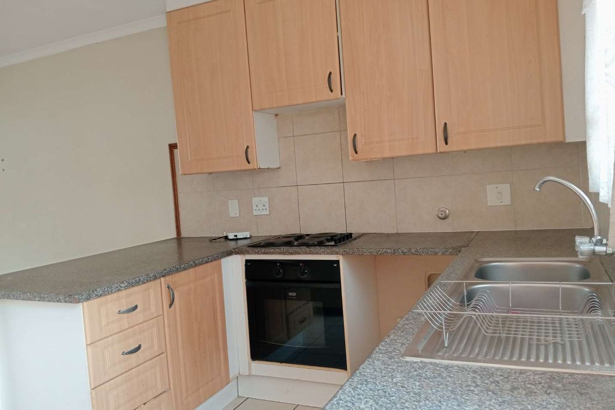A functional kitchen featuring light wood-finish cabinetry, granite-look countertops, a built-in oven with gas hob, and a double stainless steel sink.