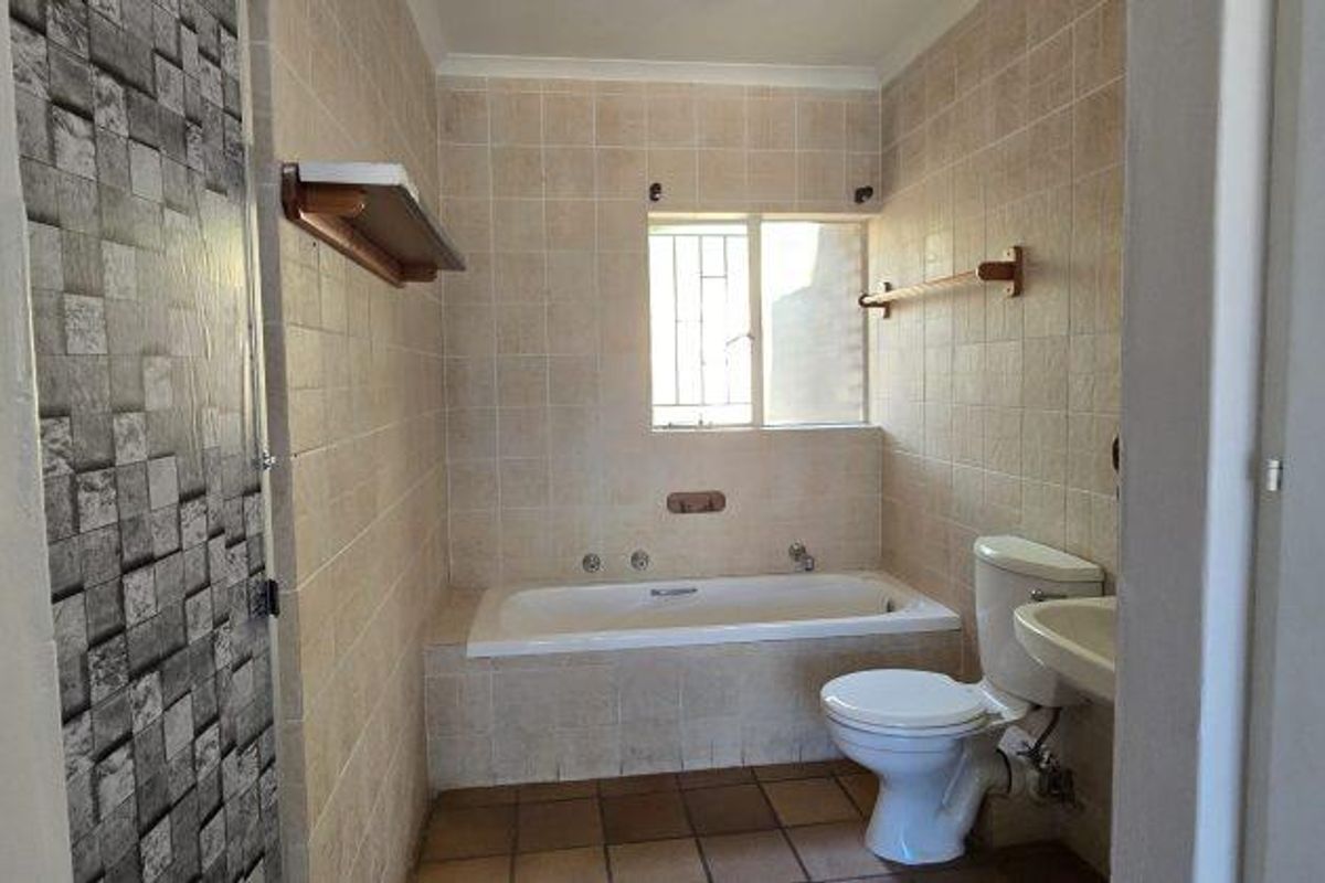 A functional bathroom featuring a built-in bathtub, standard toilet, and wall-mounted basin with neutral tiled walls and flooring.