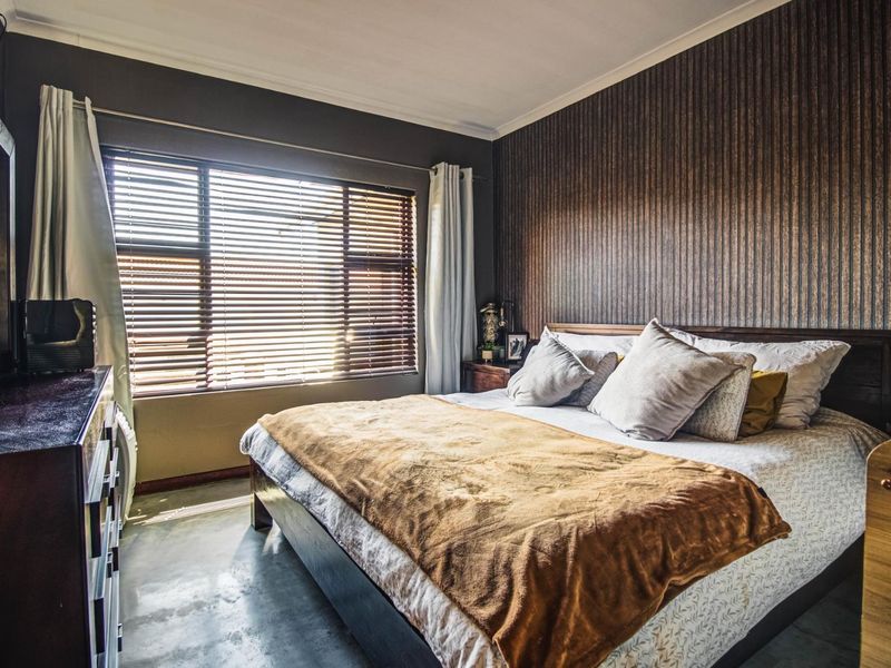 A well-maintained bedroom featuring polished concrete flooring, textured accent wallpaper, and large windows fitted with venetian blinds for natural light control.