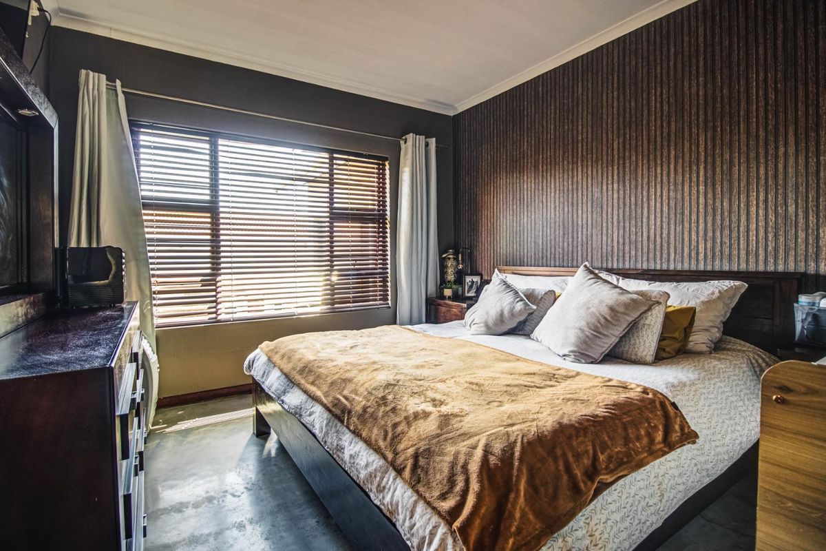A well-maintained bedroom featuring polished concrete flooring, textured accent wallpaper, and large windows fitted with venetian blinds for natural light control.